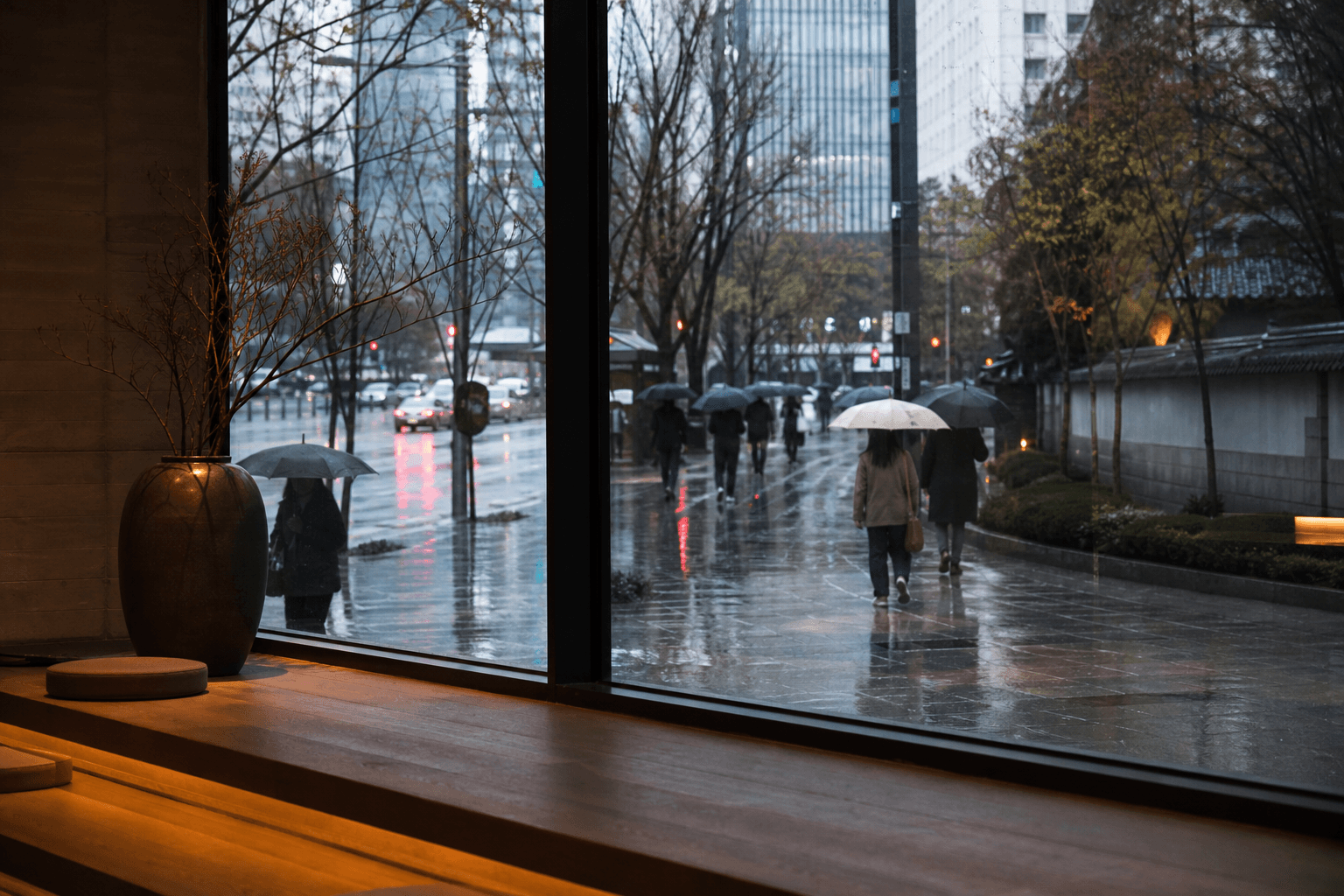 A view through a café window of people walking with umbrellas along a rainy Seoul street